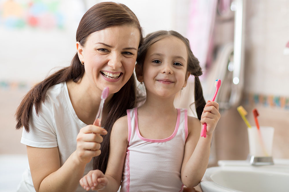 smiling mother and daughter with toothbrushes
