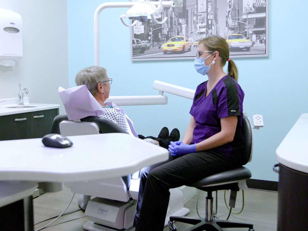 masked hygenist sitting next to patient in dental chair
